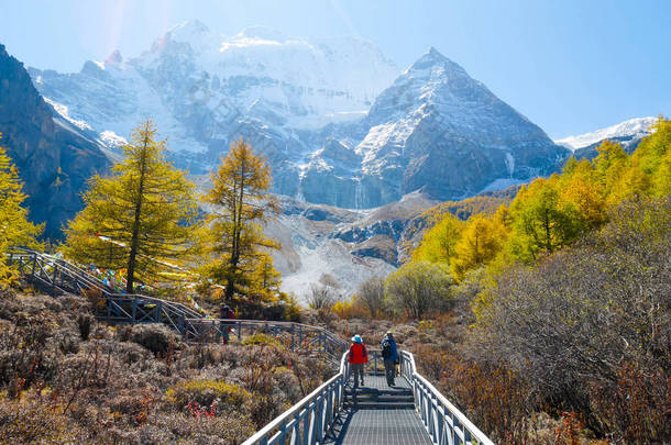 在中国四川亚丁自然保护区, 以雪山为背景的走在雪山人行道上的游客