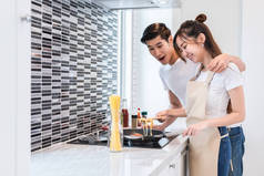 亚洲情侣或情侣在厨房里做晚餐。男人指的是女人做的美味的食物。假期和蜜月的概念。快乐甜蜜家庭主题
