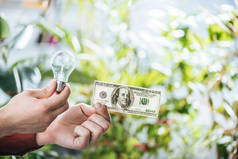 裁剪视图的人拿着一百元钞票和领导灯在手, 能源效率的概念