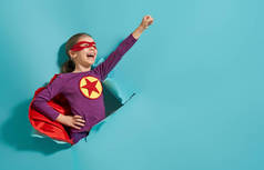 小孩在扮演超级英雄。孩子在明亮的蓝色墙的背景。女孩力量概念.