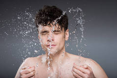 handsome man splashing water into face in the morning, isolated on grey