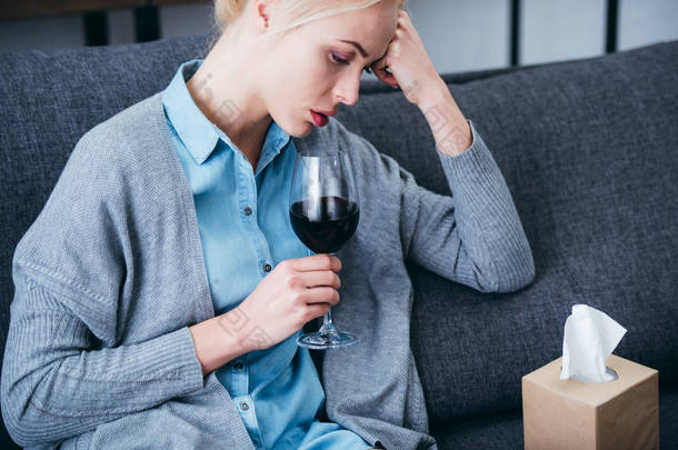 心烦意乱的女人坐在家里喝了一杯红酒和纸巾盒