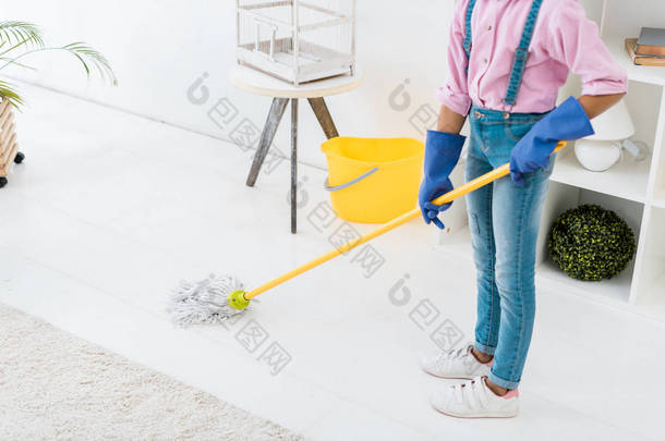 部分看法非洲裔美国女孩在蓝色橡胶手套洗涤地板与扫帚