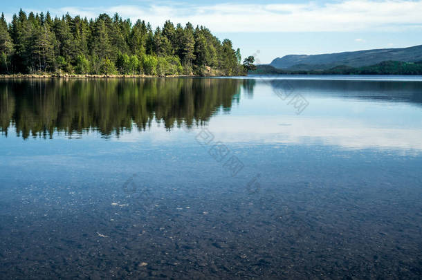 一个安静的宁静的夏日<strong>早晨</strong>, 可以看到晶莹平静的湖面上的鹅卵石, 底部的绿色森林在<strong>水面</strong>上, 地平线上有山--在大自然中的无声冥想和娱乐的概念.