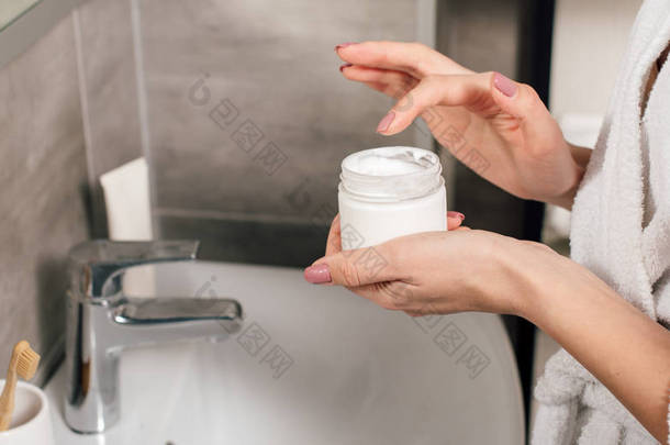 妇女拿着容器与化妆水在浴室的全景照片
