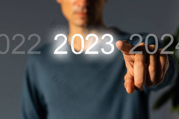 手指在灰色背景的虚拟界面上按蓝色启动2023按钮，并为文本提供复制空间。新年的概念。商人在2023年开业。新春2023年开始