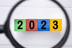 2023数字彩色木制立方体与放大镜与白色背景。新年概念.