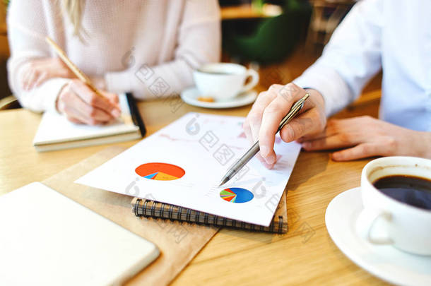 两个无法识别的商业人士的特写在咖啡桌边坐着喝咖啡的时候, 在财务报告中浏览图表