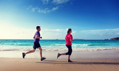 男子和妇女在日落时在热带海滩上奔跑