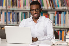 快乐的非洲男性学生在图书馆中的笔记本电脑