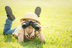 幸福微笑的孩子戴着帽子用双筒望远镜在花园里玩