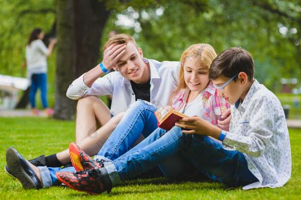 微笑的孩子在草地上玩得开心，看书。夏季，孩子们在户外玩耍。青少年在户外交流