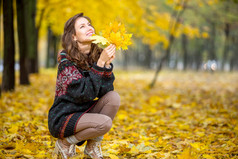秋季时装。在针织秋天的衣服，在黄色的树叶，周围公园的秋天女人。女孩，放松享受大自然