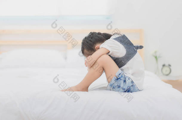 坐在床上，她抱着膝盖在难过的时候喜怒无常的郁闷亚洲小女孩.