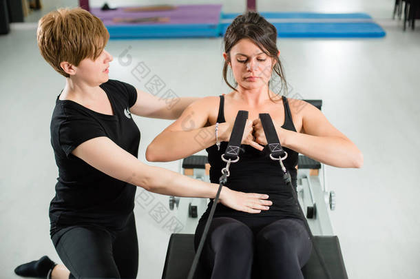 年轻适合妇女在普拉提装置改革与女<strong>讲师</strong>在空健身房锻炼。运动器材。积极健康的生活方式