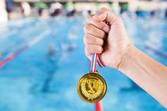 少数亚洲男子拿着金牌与游泳池和游泳比赛模糊背景.