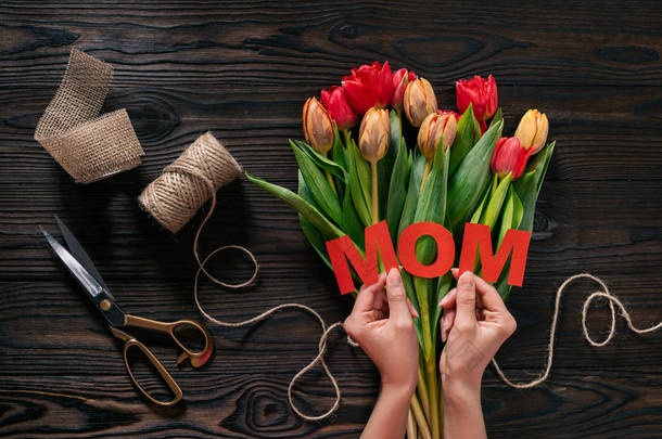母亲的部分看法在手和郁金香在木桌上的花束, 母亲节概念的妇女
