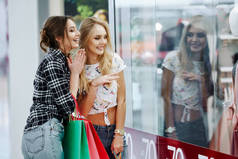 美丽的年轻妇女与五颜六色的购物袋看商店橱窗在购物中心
