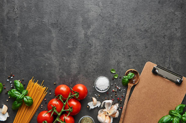 美食背景为美味的意大利菜与西红柿。各种烹调配料用勺子和空白纸板剪贴板的菜单或食谱。具有复制空间的顶部视图.