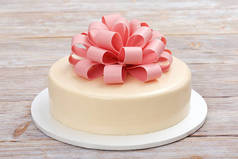 蛋糕与巧克力弓在一个木质背景关闭视图。用粉红色的巧克力蝴蝶结装饰的带有光镜釉的蛋糕。食用弓.