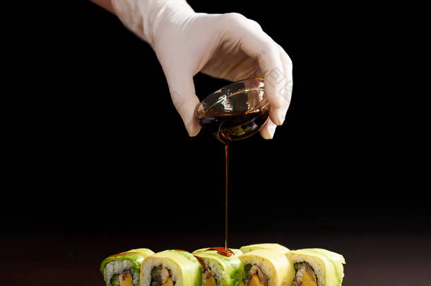 滚动寿司制作过程的特写视图。手手套倒入美味的新鲜面包酱。深色背景