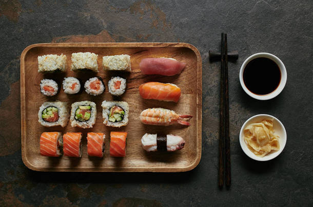 在深色桌面上的碗中, 用木<strong>盘子</strong>、<strong>筷子</strong>、姜和酱油做成的各式寿司的顶级视图