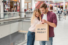 年轻夫妇的购物者向下看和手持纸袋黑色星期五在购物中心