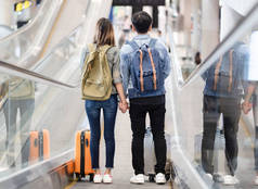 愉快的爱亚洲夫妇旅行与行李下车的自动扶梯到机场的出发区。情人旅行和运输概念.