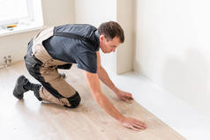 男性工人在温暖的薄膜箔地板上安装新的木质层压板地板。复合地板下的红外地板采暖系统