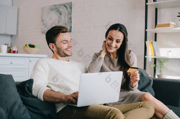 幸福的年轻夫妇在家里的沙发上用笔记本电脑做电子购物