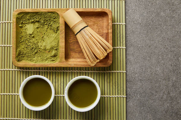 在木板上用竹须在木板上，靠近白杯，桌垫上绿茶的绿色火柴粉的顶视图