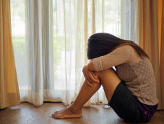 黑色和白色的伤心女人拥抱她的膝盖和哭泣。悲伤的女人独自坐在窗户或门旁边的空房间