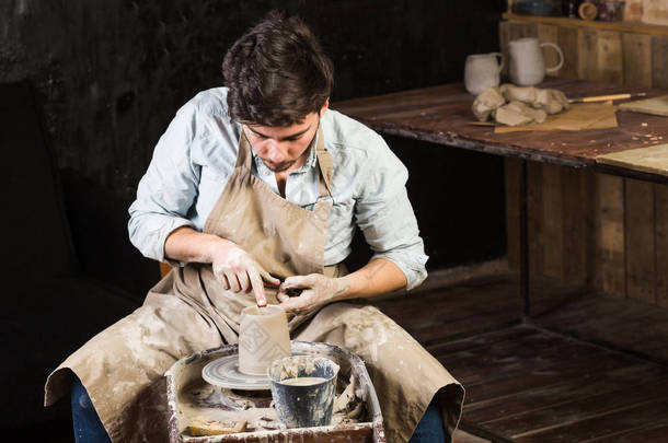 陶器、 车间、 陶瓷艺术概念-年轻男性大师作品用手和波特轮，布鲁内特的男性手指造型一些新的水罐，从原料粘土与水，特写.