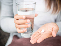 特写女人手丸成药片剂与杯水给治疗头痛。医疗保健、 医疗补充概念