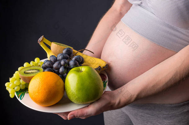 孕妇腹部拿着盘子里的水果。为控制体重和怀<strong>孕期</strong>间的健康饮食概念