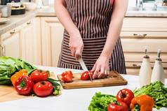 年轻的女人在家里的厨房里做饭。一个女人用小刀切番茄和蔬菜.