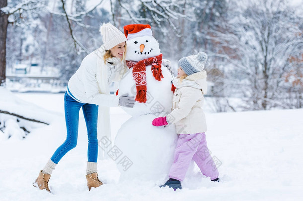 快乐的母女一起在冬天的森林里<strong>堆雪人</strong>