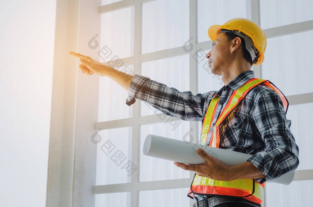 中年亚洲建筑师, 工程师或技术员男子与安全头盔持有蓝图和指点手指在建筑工地建设, 以迎接启动项目, 业务, 行业概念