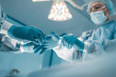 护士帮助外科医生戴医用手套的裁剪图像
