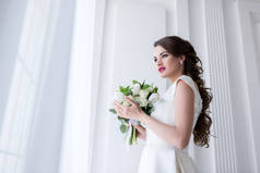美丽的年轻新娘与婚礼花束看窗口
