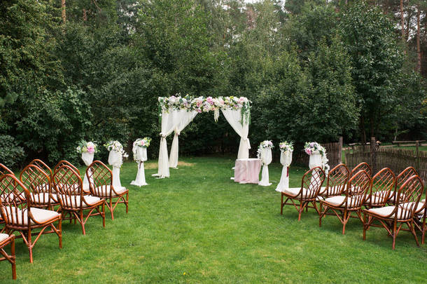 美丽的平台, 在开放的天空下举行婚礼: 在绿色的草地上的木椅, 方形的拱门装饰着鲜花