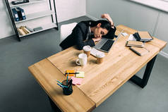 高视角的过度劳累的商人睡在工作场所与笔记本电脑和咖啡去办公室