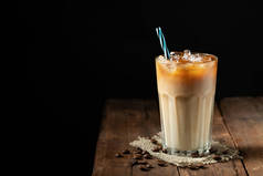 冰咖啡在一个高大的玻璃与奶油倒在和咖啡豆在一个古老的质朴的木桌上。冰冷的夏日饮料, 在黑色的木质背景上复制空间