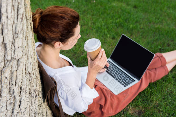 用纸杯咖啡在草地上工作的年轻妇女的<strong>高角度视图</strong>