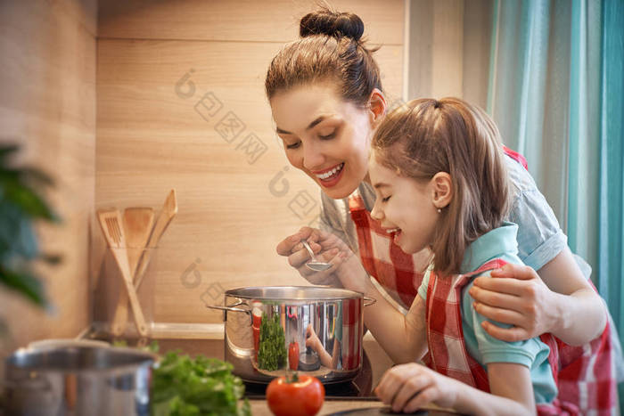 健康的食物在家里。幸福的家庭在厨房里。母亲和孩子的女儿正在准备炊具.