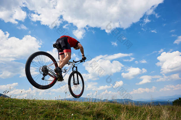 运动运动员骑自行车在专业运动衫和头盔跳跃骑脚踏车与天空和遥远的山在背景下, 户外极限运动概念