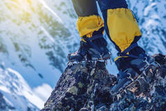 登山者在冰镐站立在山顶的入口前面的岩石在雪山的背景。脚关闭。旅游路径的概念与实现目标
