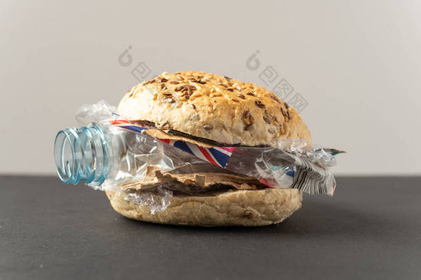 新鲜美味的汉堡与塑料废料和纸纸板在黑暗的背景。食物概念中的循环再造废物