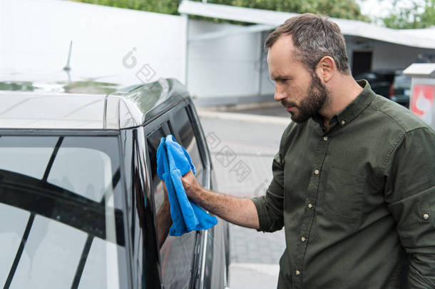 英俊男子的侧面视图清洗车窗在洗车用抹布
