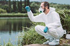 男性科学家在防护服中的侧面观察试验瓶中水样品的检测